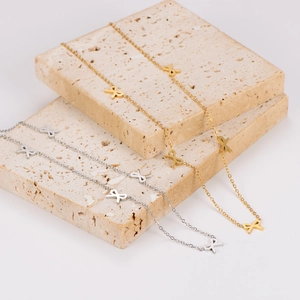Elegant gold and silver stainless steel bow necklaces set against stone backdrop