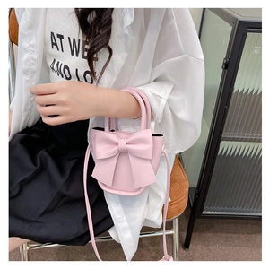 Detailed view of pink mini handbag with large bow decoration held by fashion model