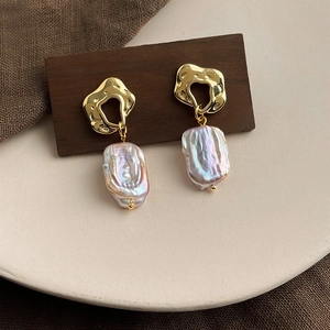 Detailed macro shot of baroque irregular pearl earrings with golden liquid metal accents