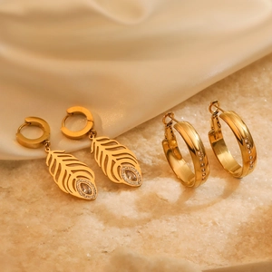 Elegant gold feather leaf drop earrings and crystal hoops on luxury silk background