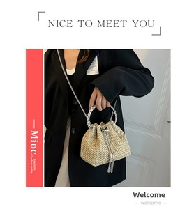 Detail of beige straw bucket bag with gold chain strap and chic ring handle
