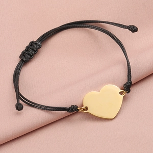 Detailed macro of a polished gold heart pendant on a black braided cord bracelet