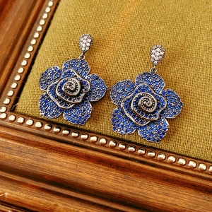 Detailed close-up of blue pavé flower earrings on vintage wooden frame background