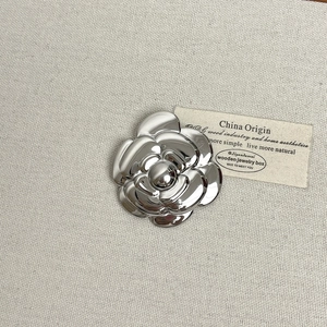 Detailed macro view of silver camellia brooch with layered metallic petals and glossy finish
