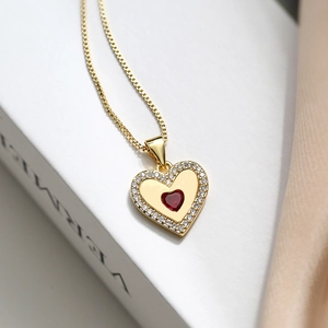 Detail of gold heart pendant with red gem and white zircon pavé on a box chain