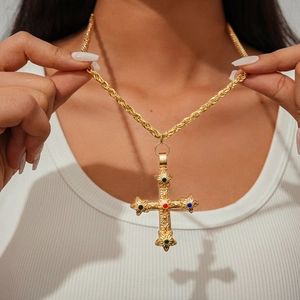 Gros plan d'un collier croix doré vintage avec gemmes colorées porté par un mannequin