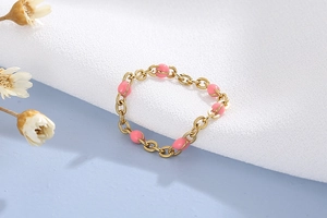 Dettaglio anello a maglia dorata con perline di resina rosa e finitura smaltata