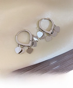 Macro shot of silver heart charms on hoop earrings against a champagne silk background