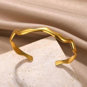 Detail of golden wave-shaped cuff bracelet with matte finish on textured stone