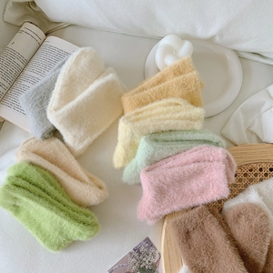 Flat lay of soft faux mink fleece socks in various pastel colors on white bedding