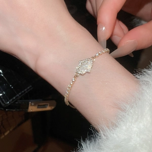 Detailed view of a gold Hamsa hand bracelet with white zircons worn on a wrist