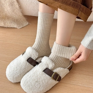 Detail of white faux shearling mules featuring brown leather strap and buckle on feet