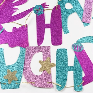 Detail of mermaid party banner with purple and teal glitter letters and shell icons