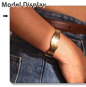 Detailed view of a wave textured 18K gold plated open bangle on a female wrist