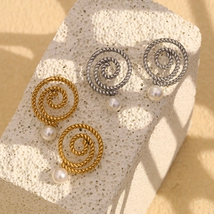 Close-up of gold and silver twisted hoop earrings with white pearl pendants on stone