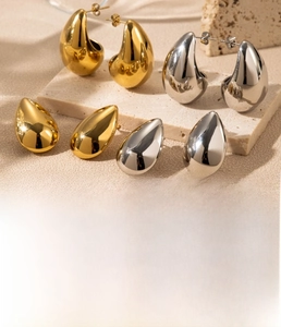 Macro shot of minimalist teardrop earrings in gold and silver finish on a stone tray