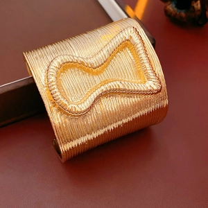 Detailed macro of gold-tone wide open cuff bracelet with vertical linear textures