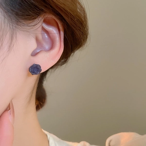 Détail d'une boucle d'oreille rose en résine foncée portée sur le lobe d'oreille