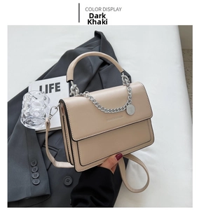 Detail of dark khaki crossbody bag with silver chain and metal pendant on bed