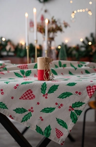 Close-up of Christmas holly leaves and red berry prints on a beige linen tablecloth