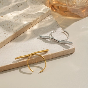 Minimalist wavy open rings in gold and silver finish on natural stone background