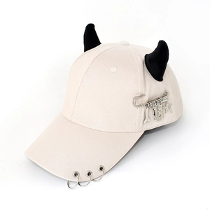 Detail of beige baseball cap featuring black demon horns and punk metal ring accessories