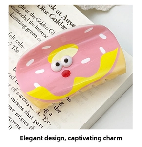Detail of pink donut-shaped hair claw clip with 3D eyes resting on an open book