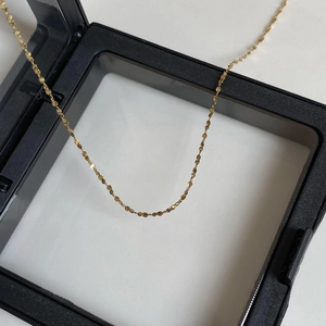 Close-up of golden shimmer chain necklace displayed on a minimalist black jewelry box