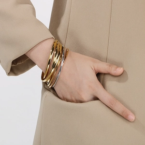 Close-up of mixed gold and silver tiered bangles worn with a camel-colored suit