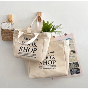 Detail view of two beige canvas tote bags with black typography hanging on a wooden hook
