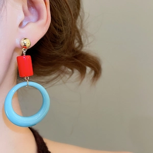 Close-up of geometric resin drop earrings with red cylinder and blue ring on model