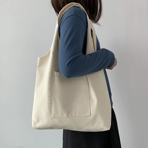 Side view of a beige canvas shoulder bag with external pocket worn by a model