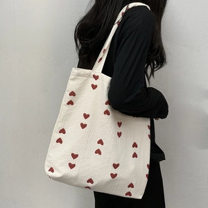 Minimalist cream textured tote bag with red heart pattern shown from a side angle