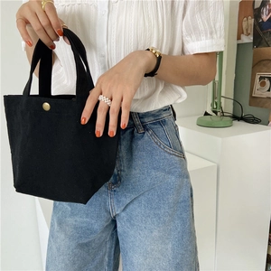 Detail of a black canvas mini handbag featuring a vintage gold metal snap button closure