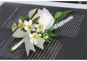 Macro shot of white rose boutonniere with green leaves and cream ribbon for weddings