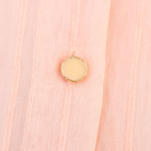 Detalle macro de botón amarillo con borde dorado en tela de blusa con rayas rosas