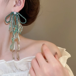 Detail of green rhinestone bow earrings with long tassels on female model