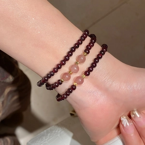 Close-up of layered garnet and strawberry quartz bracelets on wrist with gold spacers