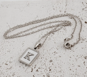 Detailed view of silver necklace with square white shell pendant featuring letter K