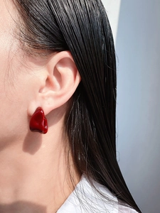 Close-up of model wearing deep red irregular enamel stud earring in modern abstract style