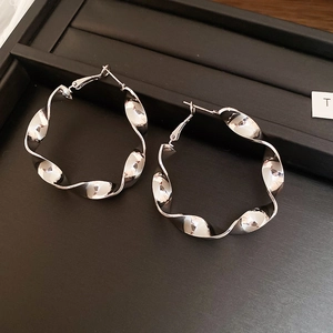 Détail de créoles torsadées argentées au fini poli brillant sur un plateau d'exposition noir