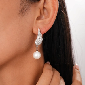 Close-up of silver wing earrings with micro-set diamonds and dangling white pearl