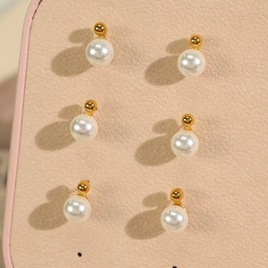 Three pairs of white round pearl earrings with gold bases on beige leather background