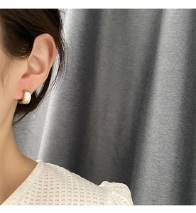 Detail of gold U-shaped earring with white mother of pearl inlay worn by a model