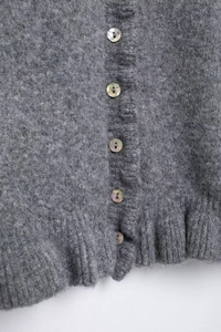 Detailed close-up of grey knit cardigan featuring iridescent shell buttons and ruffled hem