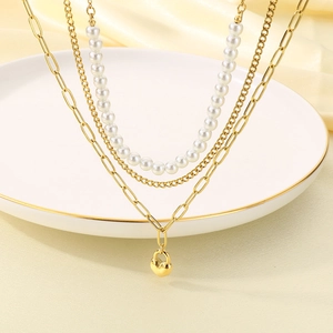 Close-up of layered gold necklace with faux pearls and heart lock pendant on white porcelain