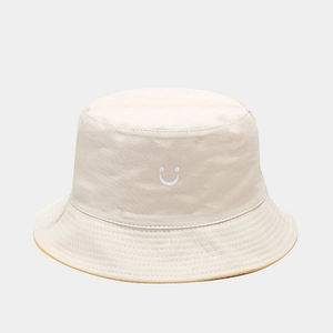 Detail of a beige reversible bucket hat with yellow interior and smile embroidery