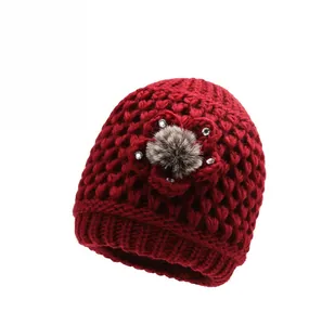 Detailed knit texture of red winter hat featuring a decorative floral accent and fur pom