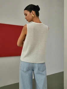 Chic cream hollow-out knit vest top paired with blue jeans in a minimalist studio setting