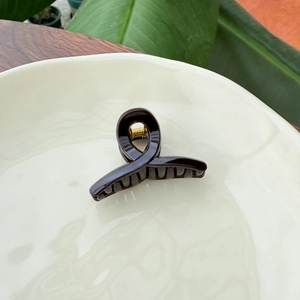 Detailed top view of a dark brown glossy hair claw clip on a white ceramic plate